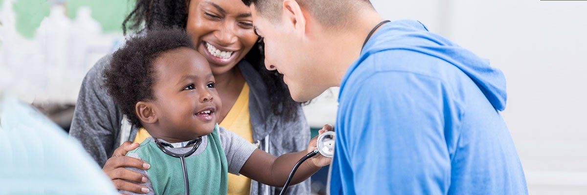 Health Equity. Latino doctor examining African-American child on mother's lap who is playing with the doctor's stethoscope.